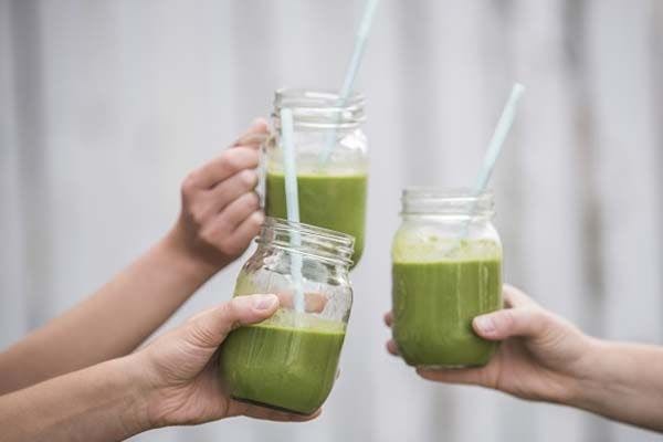 A group of three friends cheersing each other with green smoothies in their hands. 